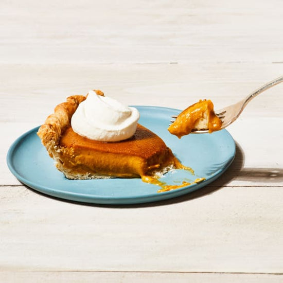 slice of kabocha squash pie on a blue plate with whipped cream and a fork taking out a bite
