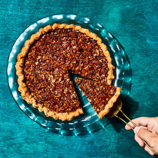 hand pulling out a slice of pecan pie in a glass pie plate on blue background